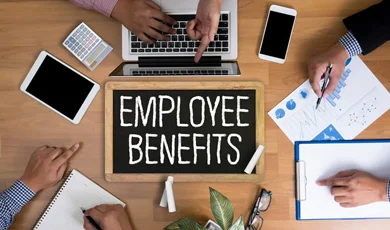 employees gathered around table working with employee benefits sign written in chalk