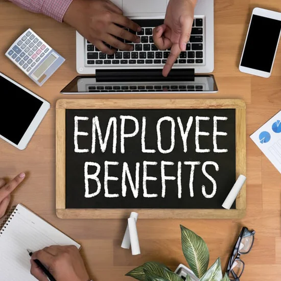 employees gathered around table working with employee benefits sign written in chalk