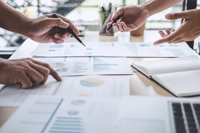 business colleagues discussing reports and analytics spread across desk business colleagues discussing reports and analytics spread across desk