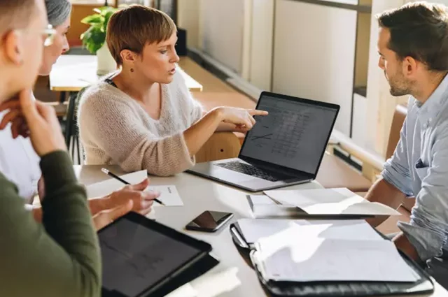 businesswoman in meeting sharing reports on laptop to coworkers