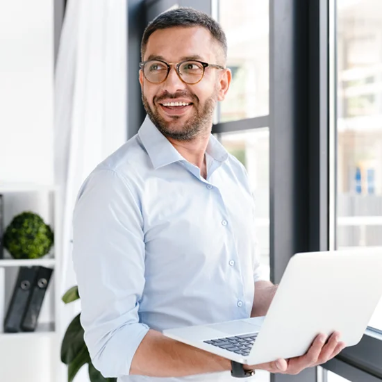 male businessman holding laptop in front of window male businessman holding laptop in front of window
