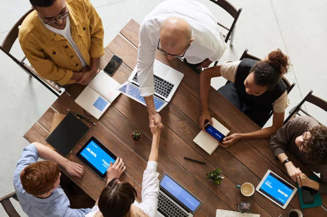 diverse group of professionals is seated around a conference table communicating, engaged in a meeting