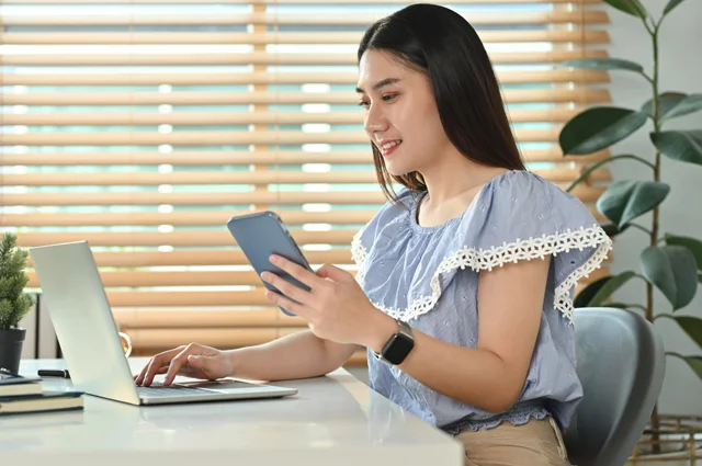young business woman holding smart phone while working on laptop
