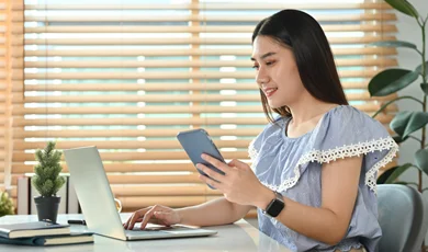 young business woman holding smart phone while working on laptop