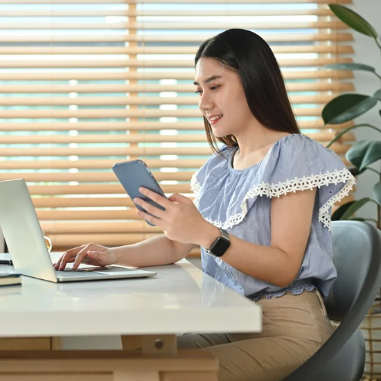 young business woman holding smart phone while working on laptop