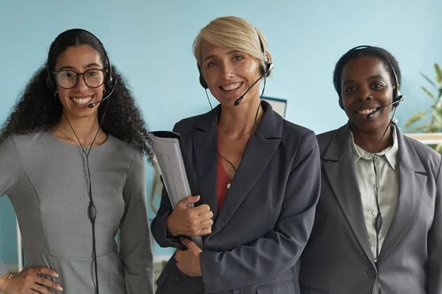 three women are smiling and wearing headsets and business attire