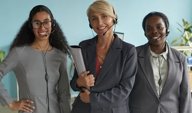 three women are smiling and wearing headsets and business attire
